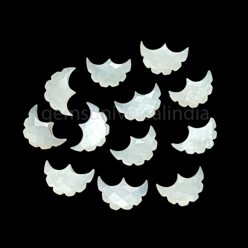 May include: A collection of 12 white mother of pearl crescent moon shaped cabochons. The cabochons are approximately 1 inch in length and have a slightly iridescent finish.