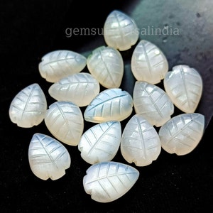 May include: A collection of 15 white moonstone leaf shaped cabochons. The cabochons are carved with a leaf design and have a translucent, milky white color.
