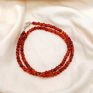 Puede incluir: Un collar de doble cadena hecho de cuentas de cornalina. Las cuentas son de color naranja intenso y est&aacute;n enhebradas en una cadena de plata.