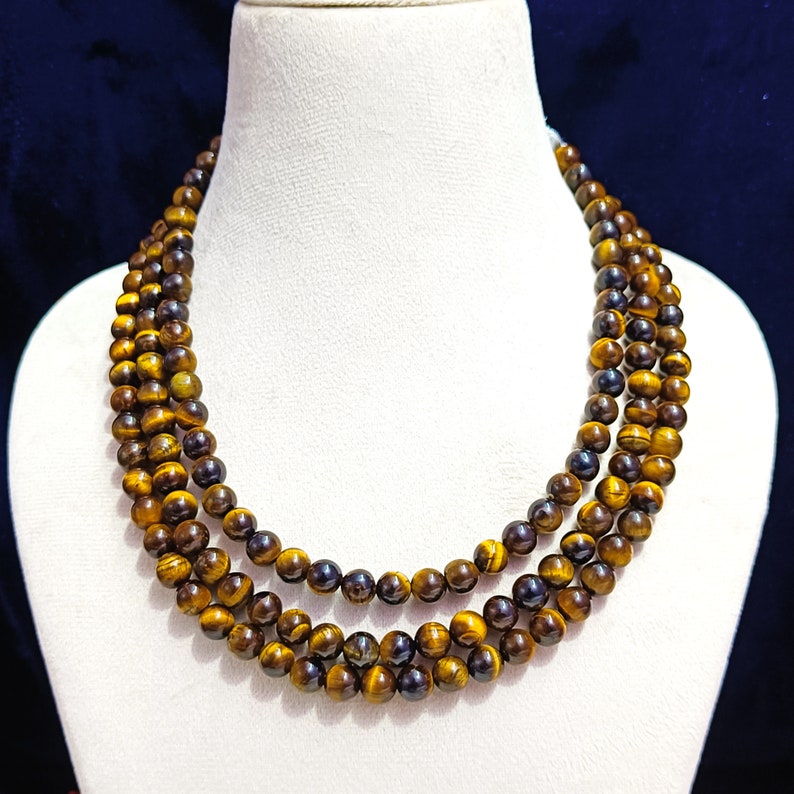 May include: A three-strand necklace made of tiger's eye beads. The beads are a mix of golden brown and dark brown colors.
