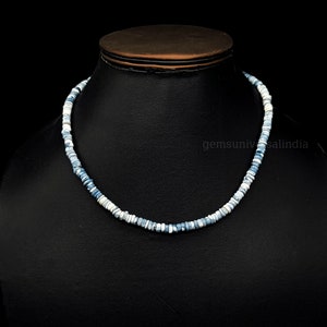 May include: A necklace made of small, round, blue and white opal beads. The necklace is on a black display stand.