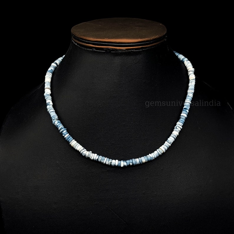 May include: A necklace made of small, round, blue and white opal beads. The necklace is on a black display stand.