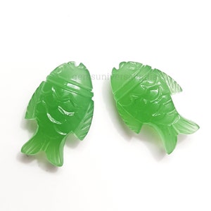 K&ouml;nnte beinhalten: Zwei gr&uuml;ne Jade-Fisch-Anh&auml;nger mit detaillierten Schnitzereien. Die Fische sind in entgegengesetzte Richtungen ausgerichtet und haben eine gl&auml;nzende Oberfl&auml;che.