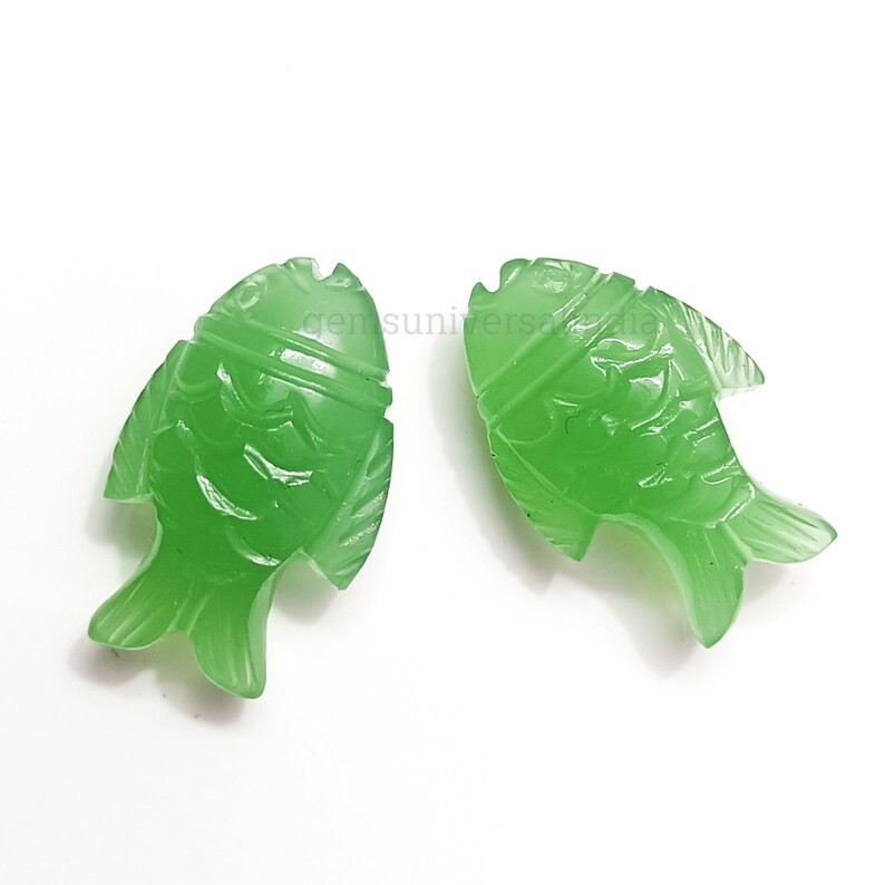 K&ouml;nnte beinhalten: Zwei gr&uuml;ne Jade-Fisch-Anh&auml;nger mit detaillierten Schnitzereien. Die Fische sind in entgegengesetzte Richtungen ausgerichtet und haben eine gl&auml;nzende Oberfl&auml;che.