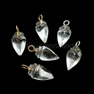 May include: Six clear glass teardrop-shaped pendants with gold-colored metal loops. The pendants are all the same size and shape, and they are arranged in a random pattern.