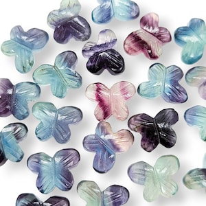 May include: Assortment of carved butterfly-shaped fluorite beads in various shades of blue, purple, and pink. The beads are made of natural fluorite and have a polished finish.