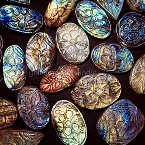 May include: A collection of oval-shaped labradorite gemstones, each carved with a detailed floral design. The stones display a range of iridescent colors, including blue, green, and gold.