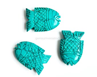 May include: Three turquoise fish-shaped carvings with intricate etched details. The fish have a vibrant teal color with dark veining, and are arranged on a white background. The carvings are likely gemstones or decorative elements.