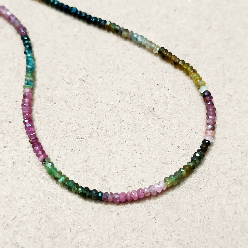 May include: A multi-colored gemstone necklace with small, round beads in shades of pink, green, and blue.