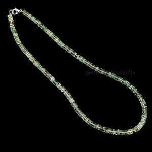May include: A green gemstone necklace made of small, square-shaped beads. The necklace is strung on a silver chain and has a silver clasp.