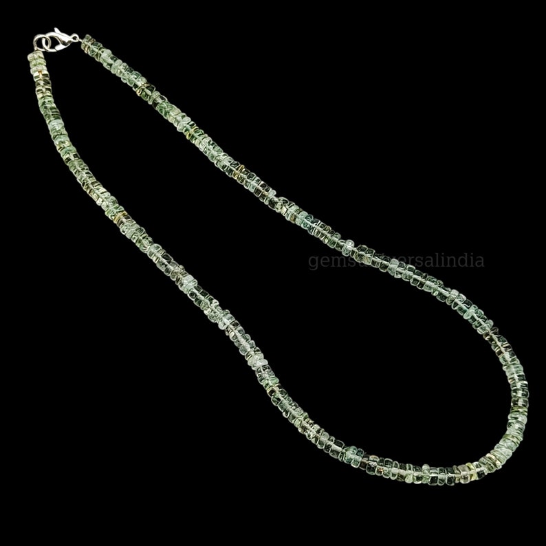 May include: A green gemstone necklace made of small, square-shaped beads. The necklace is strung on a silver chain and has a silver clasp.