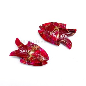 May include: Two red and gold fish carvings made of gemstone. The fish are detailed with intricate carvings and have a shiny, polished finish.