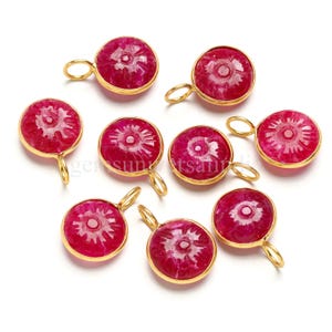 Può includere: Una collezione di otto pendenti in rubino con montature color oro. Ogni pendente presenta un disegno floreale intagliato all'interno di una forma circolare. I pendenti hanno un anello nella parte superiore per il fissaggio a una catena o ad altri componenti di gioielleria.