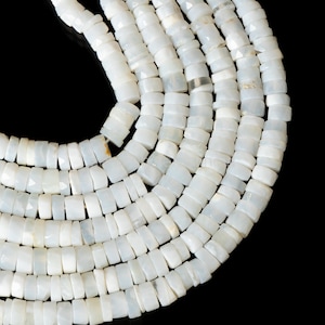 May include: Strands of white, square-cut beads, possibly gemstone or shell, arranged in a spiral against a black background. The beads have a slightly iridescent quality, reflecting light. The beads are uniform in size and shape, suggesting they are machine-cut.