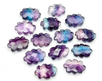 Puede incluir: Una colección de gemas facetadas en forma de nube en tonos morados, azules y transparentes. Las gemas están dispuestas sobre una superficie blanca, mostrando sus intrincados cortes y variaciones de color. Estas piedras decorativas son ideales para la fabricación de joyas.