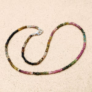 May include: A multi-colored gemstone necklace with a silver clasp. The necklace is made of small, round beads in shades of pink, green, brown, and black.
