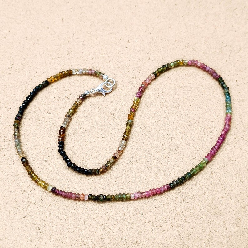 May include: A multi-colored gemstone necklace with a silver clasp. The necklace is made of small, round beads in shades of pink, green, brown, and black.