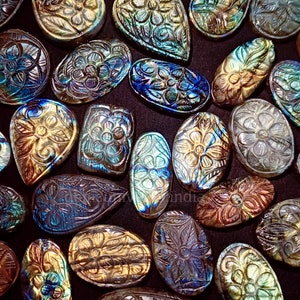 May include: Assortment of carved labradorite gemstones in various shapes and sizes. The stones are iridescent with shades of blue, green, and gold. Each stone features a carved floral design.
