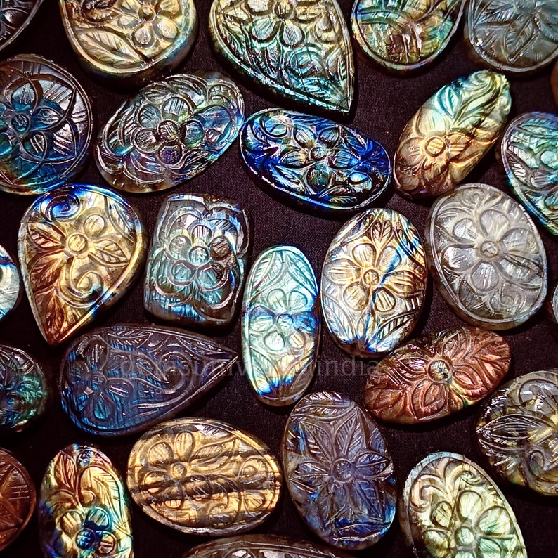 May include: Assortment of carved labradorite gemstones in various shapes and sizes. The stones are iridescent with shades of blue, green, and gold. Each stone features a carved floral design.
