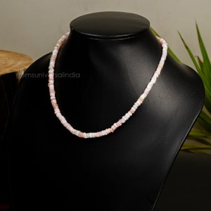 May include: A pink and white beaded necklace made of small, square-shaped beads. The necklace is displayed on a black mannequin.