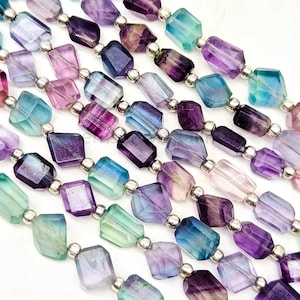 Könnte beinhalten: Eine Strähne aus facettierten Fluoritperlen in Violett-, Blau- und Grüntönen. Die Perlen sind durch silberne Abstandshalter getrennt.