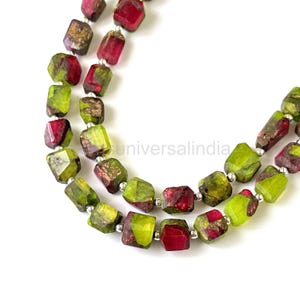 May include: Close-up of two strands of gemstone beads. The beads are a mix of green and burgundy colors, with a faceted, rectangular shape. The beads are strung together with silver-colored metal. The background is white.