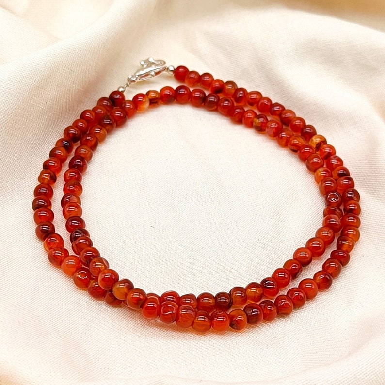 Puede incluir: Un collar de doble cadena hecho de cuentas de cornalina. Las cuentas son de color naranja intenso y tienen un acabado liso y pulido. El collar est&aacute; asegurado con un cierre de plata.