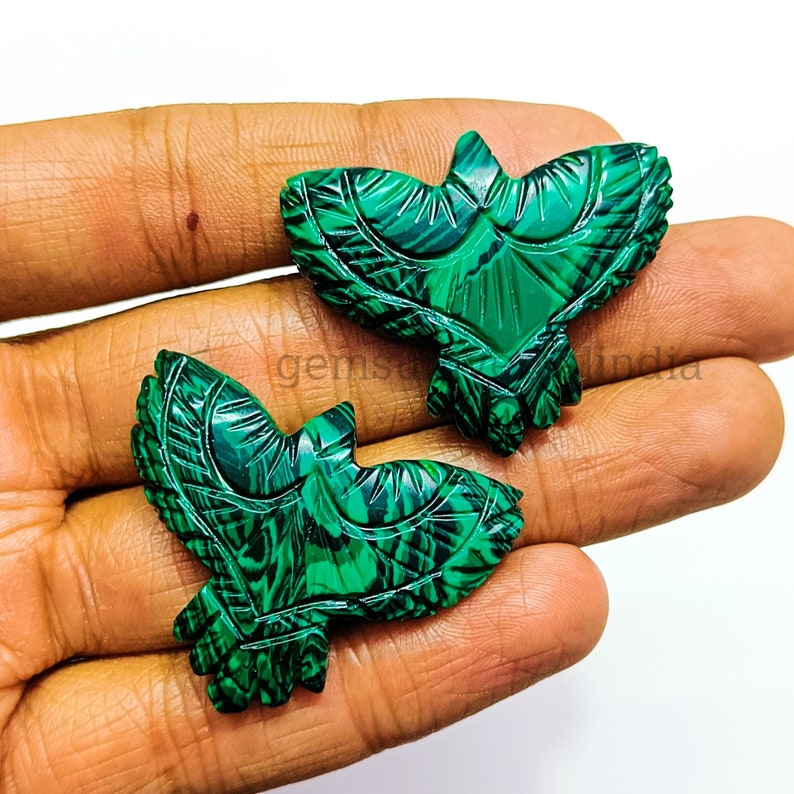 May include: Two green malachite gemstone carvings of birds with intricate details. The carvings are in the shape of birds with their wings spread out.