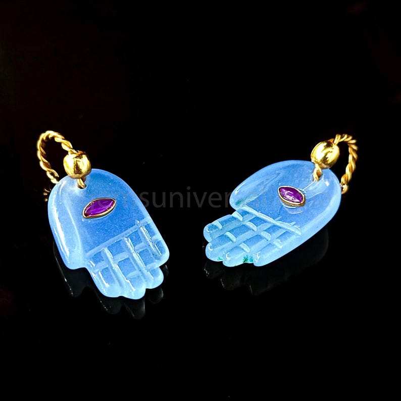 May include: A pair of blue glass earrings shaped like hands with a small red gemstone in the center of each hand. The earrings are attached to gold hoops.