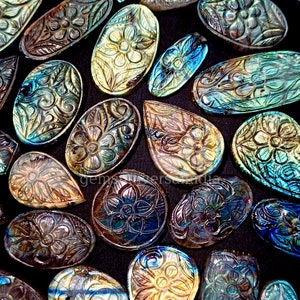 May include: A collection of iridescent labradorite gemstone cabochons carved with intricate floral designs. The stones are a mix of blue, green, and gold colors.