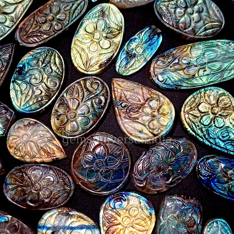 May include: A collection of iridescent labradorite gemstone cabochons carved with intricate floral designs. The stones are a mix of blue, green, and gold colors.