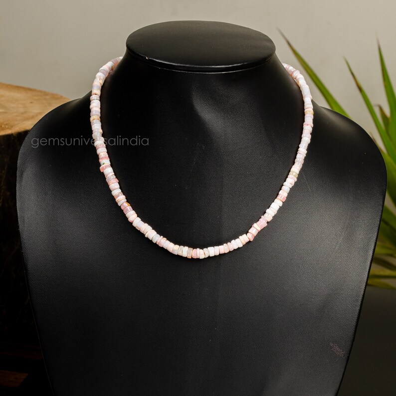 May include: A delicate necklace made of small, pink and white opal beads. The necklace is displayed on a black mannequin bust.