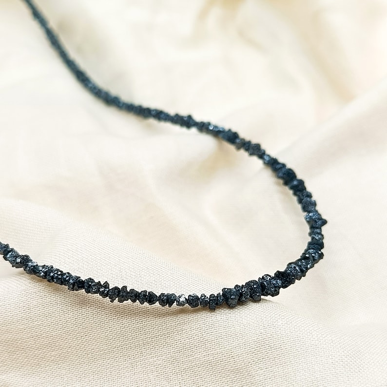 May include: A black diamond necklace made of small, rough-cut stones. The necklace is strung on a thin wire and has a simple, elegant design.