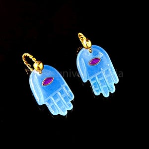May include: A pair of blue hamsa hand earrings with gold accents and a small ruby-colored stone in the center of each hand.