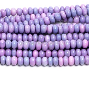 May include: Close-up of multiple strands of oval-shaped beads in shades of lavender and lilac. The beads are strung together, displaying a gradient of colours from pale pink to deep purple. Suitable for jewellery making, these beads offer a range of hues.