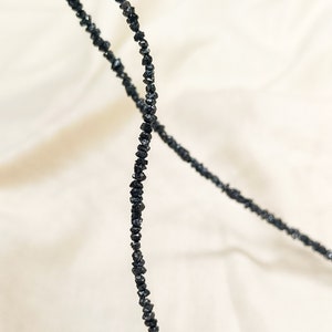 May include: A strand of black diamond beads, strung together to form a necklace. The beads are irregularly shaped and have a rough, natural texture.