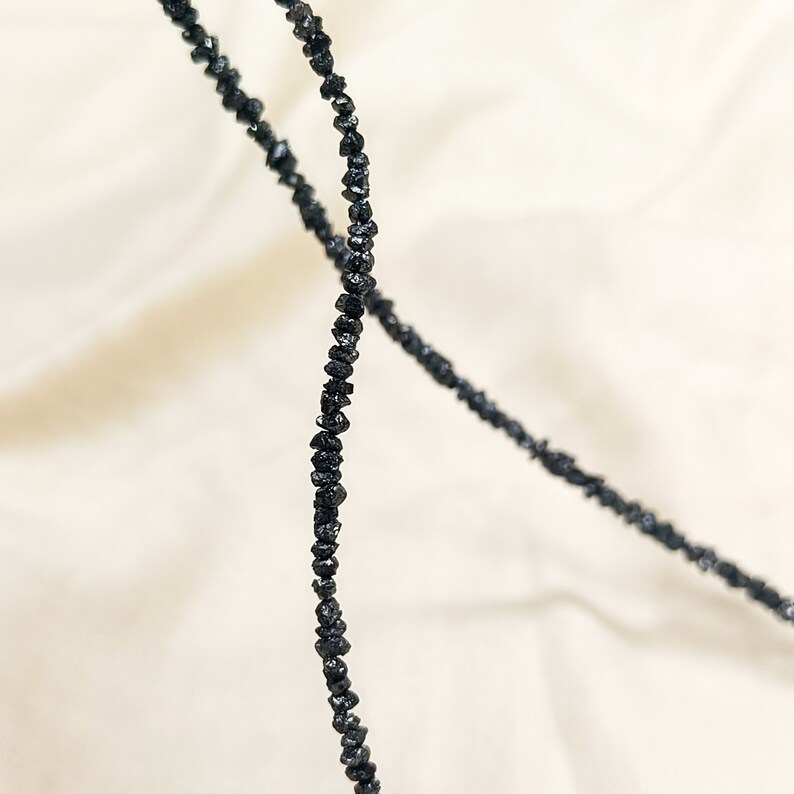 May include: A strand of black diamond beads, strung together to form a necklace. The beads are irregularly shaped and have a rough, natural texture.