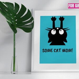 Puede incluir: Un gato negro con ojos grandes y sus patas levantadas en el aire, impreso sobre un fondo azul. El texto "SOME CAT MOM!" está impreso debajo del gato. La imagen está enmarcada en un marco blanco.