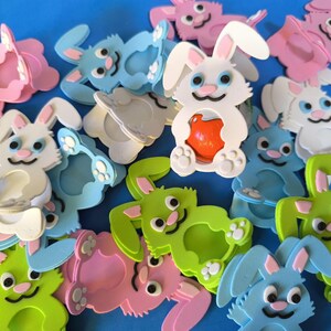 May include: A collection of colorful foam bunny-shaped party favors. The bunnies are in various colors, including pink, blue, green, and white. Some of the bunnies have a small hole in the center, while others have a small hole in the center and a small red ball inside.