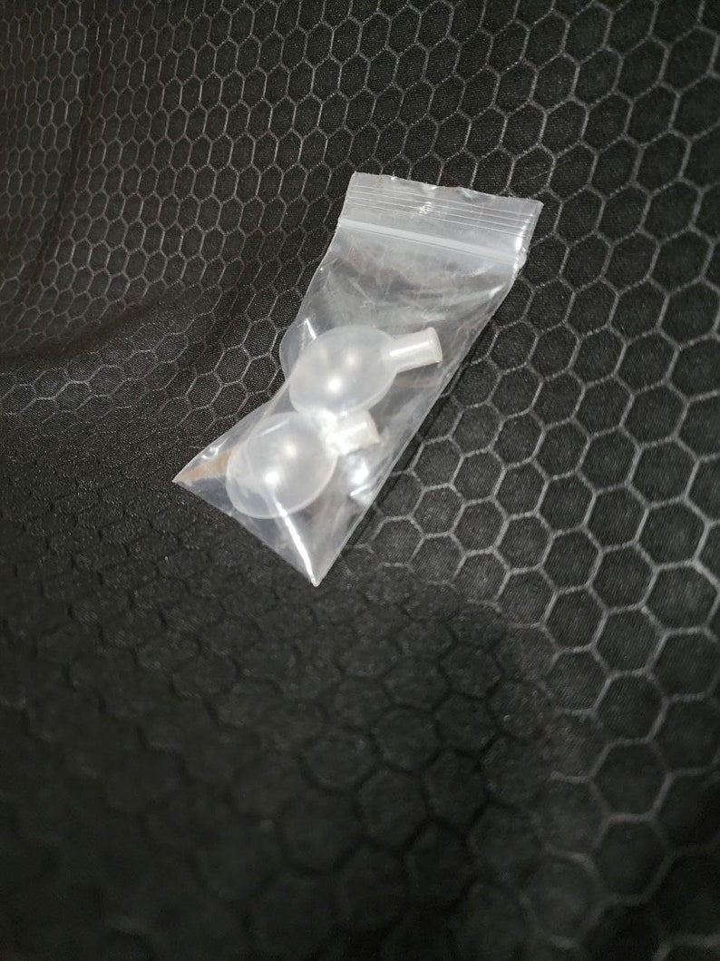 Op de afbeelding: Twee transparante plastic piep-speelgoed voor honden in een transparante plastic zak. De speelgoed zijn rond met een klein gat aan de bovenkant voor een pieper.
