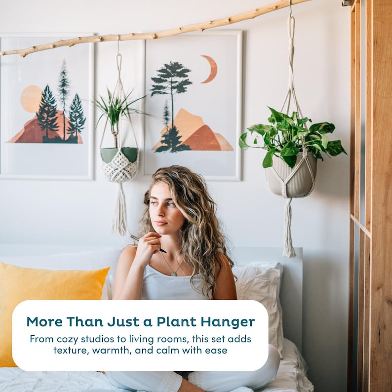 May include: A woman sits on a bed with a yellow pillow, looking towards hanging plant holders. The plant holders are suspended from a wooden branch, with three framed landscape art prints in the background. The text in the image reads: "More Than Just a Plant Hanger."