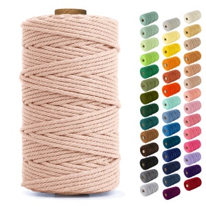 May include: A spool of thick, natural cotton rope in a light pink color. The rope is wound tightly around the spool, creating a smooth, even surface. The spool is made of wood and has a natural finish.