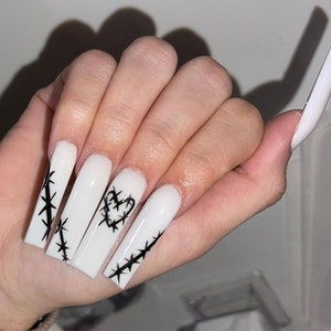 May include: Long white acrylic nails with black barbed wire designs. One nail features a barbed wire heart.