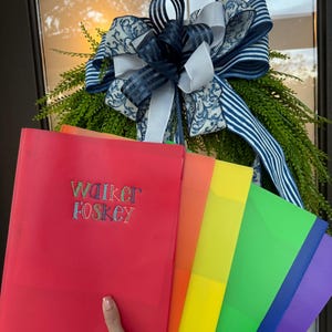 May include: A set of five translucent plastic folders in red, orange, yellow, green, and purple. The red folder features the embroidered text "WALKER FOSKEY" in a multi-colored, dotted font. The folders are arranged in a fan-like display.