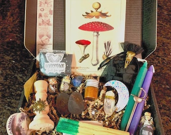Puede incluir: Una caja llena de diversos artículos de brujería, incluyendo velas, cristales, una pequeña bolsa, una perilla de madera con forma de sol, una botella de hierbas, una pequeña botella con una etiqueta de agradecimiento y una tarjeta con una ilustración vintage de un hongo.