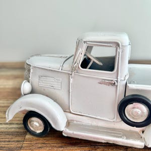 A white vintage-style truck is displayed on a wooden surface.