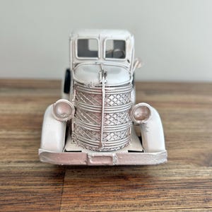 A white metal toy truck with a basket on the front, sitting on a wooden surface.