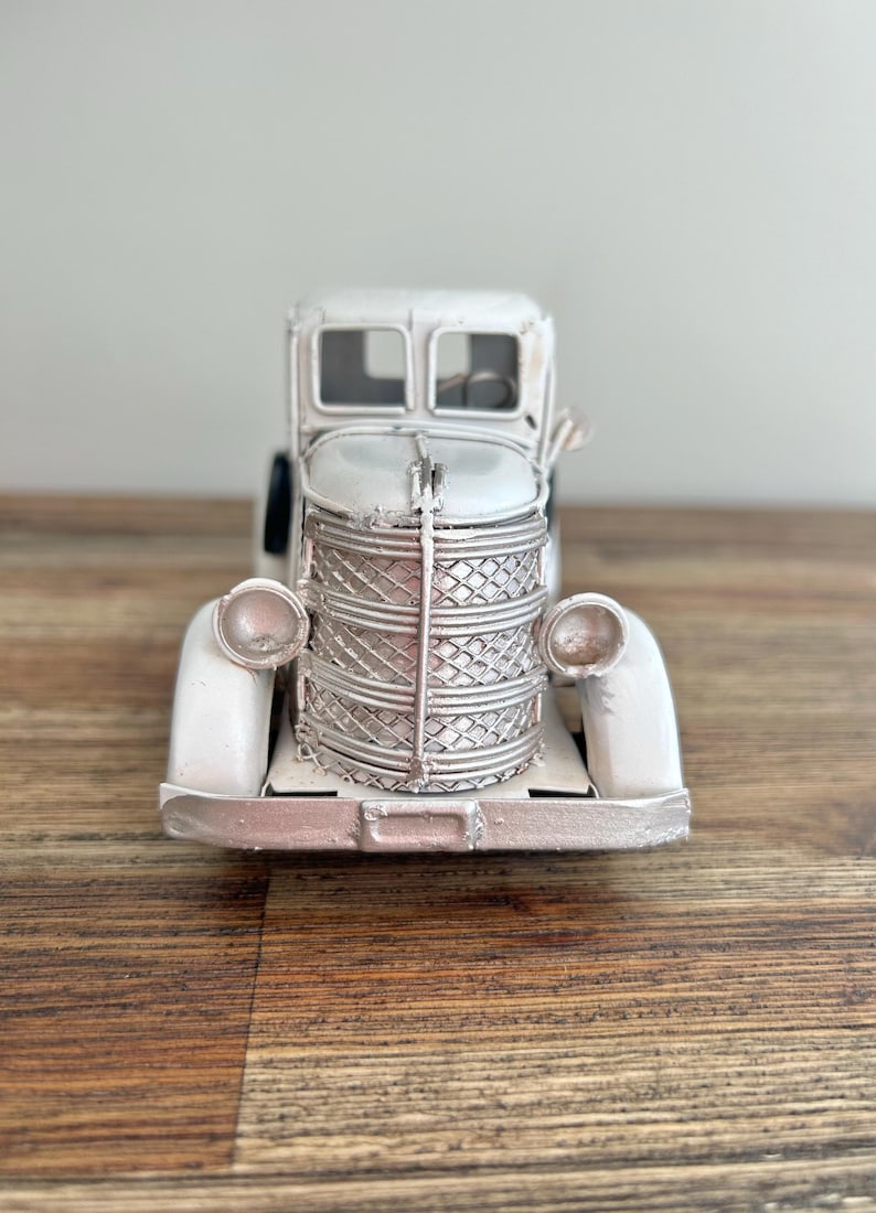 A white metal toy truck with a basket on the front, sitting on a wooden surface.