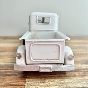 A white metal model of a vintage truck is displayed on a wooden surface.