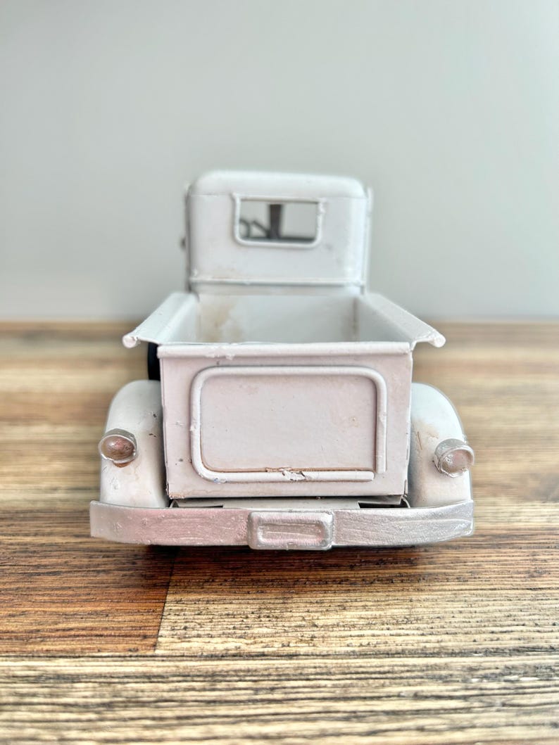 A white metal model of a vintage truck is displayed on a wooden surface.